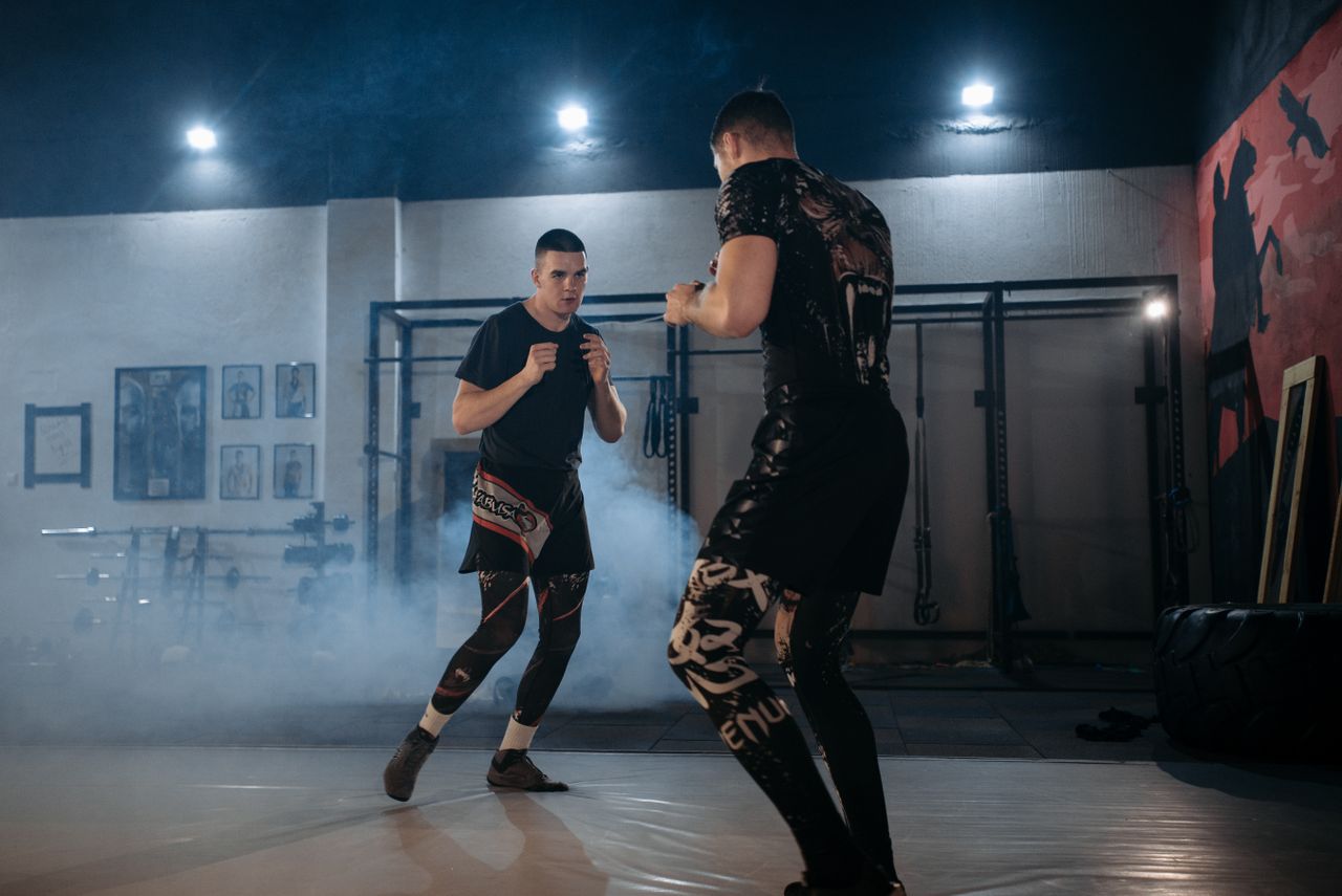 Two men engaged in a focused MMA sparring session in a gym, showcasing skill and technique.